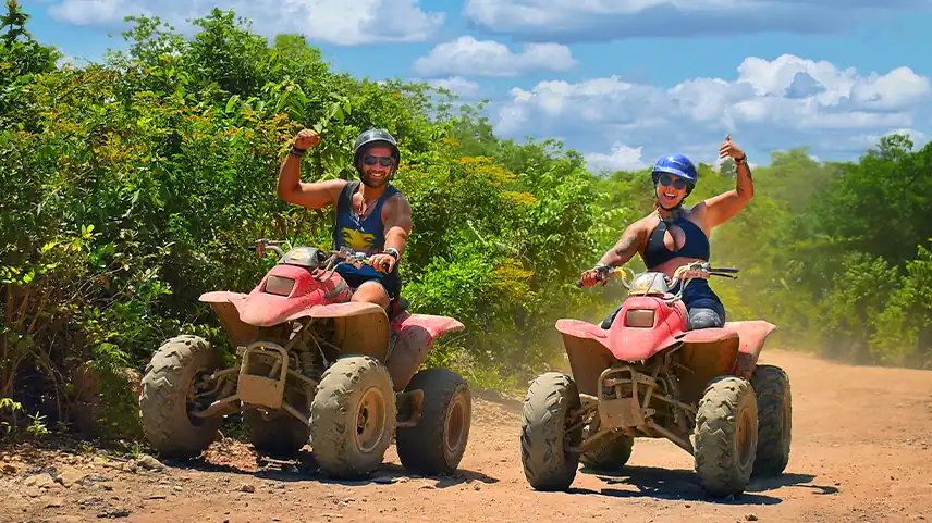 Couple striking a pose while riding red ATVs in the jungle on an extreme adventure tour in the Riviera Maya.