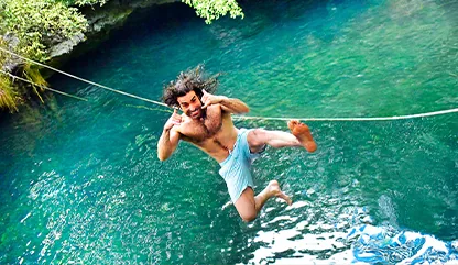 Man jumping backwards into a cenote on an extreme tour eith stunning blue crystal-clear water below.