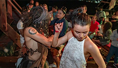 Woman with white tank top dancing at the pirate ship with other tourists dancing and having fun in the background.