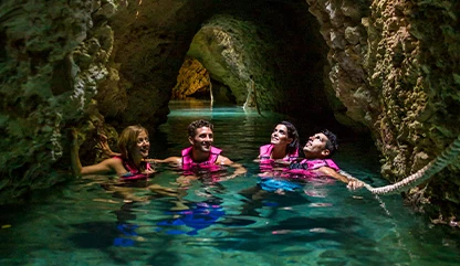 Group of friends swimming in the underground river in Xcaret, exploring the tunnels with blue crystal-clear water.