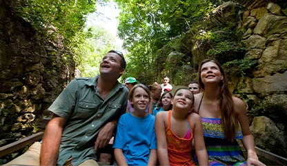 Happy family enjoing a scenic boat ride through the lush canals of Xcaret, sorrounded by towering rock walls and tropical vegetation.