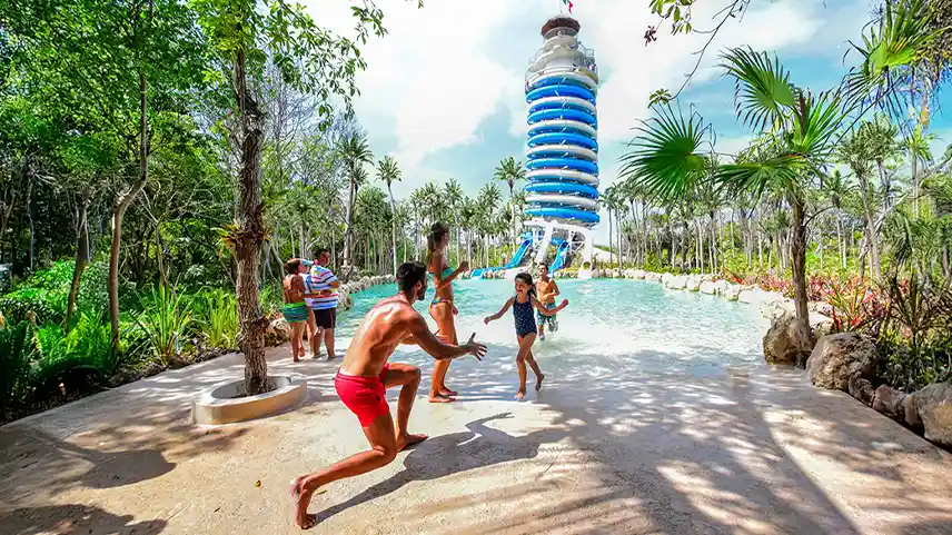 Father greeting daughter near toboggan tower at Xel-Ha, with families having fun with the magic Mayan Rainforest sorrounding the pool.