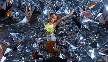 Woman wearing a yellow tank top
jumping and striking a pose in the mirror room at Xenses park.