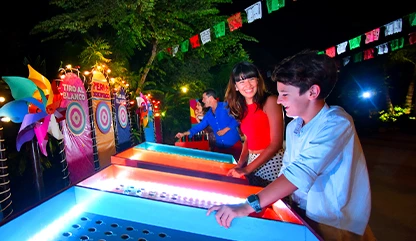 Boy and a girl playing
carnival or feria games at the Xoximilco explanada, surrounded by colorful papel picado decorations.