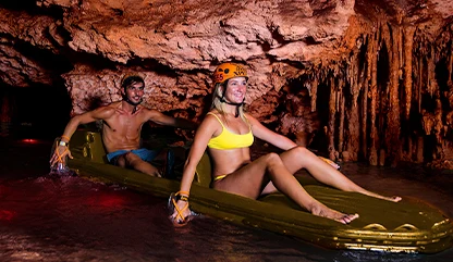 Couple in a raft paddling through a tight cave in Xplor, admiring stalactites and exploring the underground river in crystal-clear water.