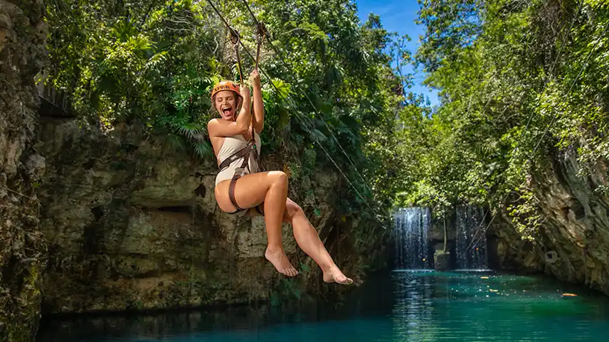 Woman in a white swuimsuit thrilled
in the zipline activity over the blue waters of Xplor eco-park.