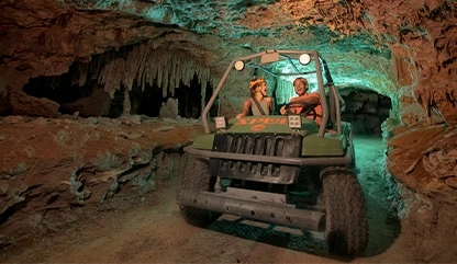 Couple exploring a cave in 4x4
cars, with stalactites hanging deep within the tunnel in Xplor's activity.