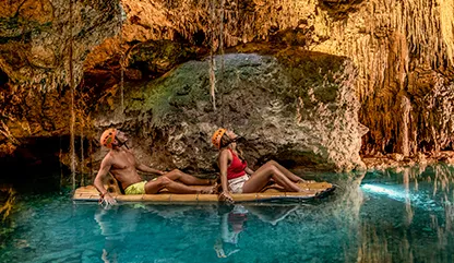 Couple in a raft paddling through
a cave in Xplor, admiring stalactites and exploring the underground river in crystal-clear water.